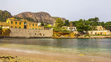 Timelapse,-small-gentle-bay-overlooking-stone-wall,-old-buildings-in-Sicily