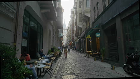Motorrad-Fährt-Auf-Schmaler-Straße-Mit-Restaurants-Und-Geschäften-In-Galata,-Istanbul