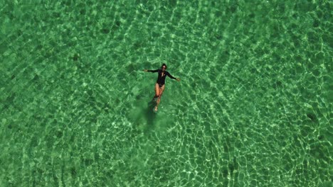Aerial-view:-Woman-in-black-swims-in-bright-green-water,-copy-space
