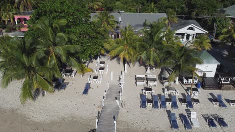 Low-aerial-orbits-over-sunny,-sandy-beach-restaurant-with-palm-trees