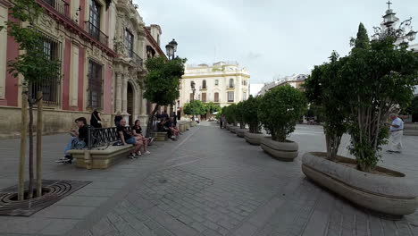 Menschen-Sitzen-Auf-Bänken-Im-Parkhof-In-Der-Nähe-Der-Catedral-De-Sevilla-In-Sevilla,-Spanien