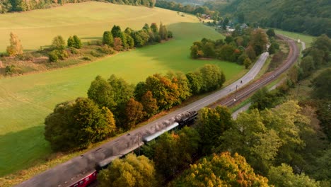 Steam-train-with-passenger-cars-driving-through-an-autumn-landscape-on-a-sunny-day