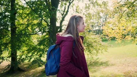 Young-girl-with-a-cheerful-smile-and-long-hair-is-walking-with-a-backpack-on-her-back-on-a-sunny-day
