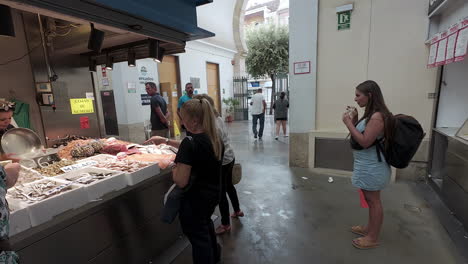 Woman-sips-her-drink-as-she-watches-the-lively-fish-market-in-the-streets-of-Seville,-Spain