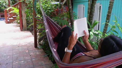 Young-brunette-woman-in-tropical-hammock-enjoys-reading-a-good-book