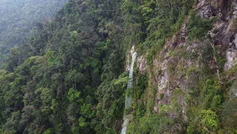 Cliff-aerial-flies-to-wispy-jungle-waterfall-in-Honduras-mountains