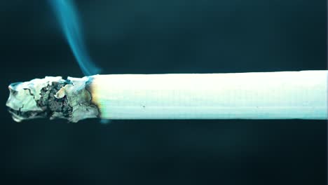 Cigarrillo-Hecho-A-Medida,-Casi-Completamente-Aislado,-Colocado-A-Lo-Largo-De-Toda-La-Toma-En-El-Medio,-De-Un-Extremo-A-Otro,-La-Ceniza-Cae-Lentamente-Consumiendo-Papel-Liberando-Humo-Azul,-Fondo-Negro.