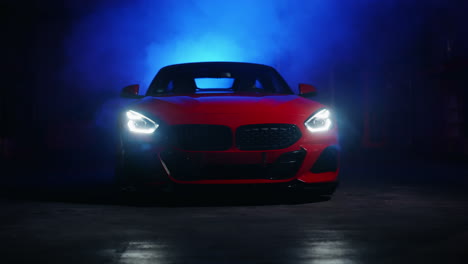 Red-sports-car-with-glowing-headlights-in-studio-light-setup-with-changing-colors-in-fog