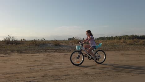 Junges-Mädchen-Auf-Ihrem-Fahrrad-Auf-Dem-Weg-Nach-Hause-Auf-Einer-Trockenen-Wüstenstraße
