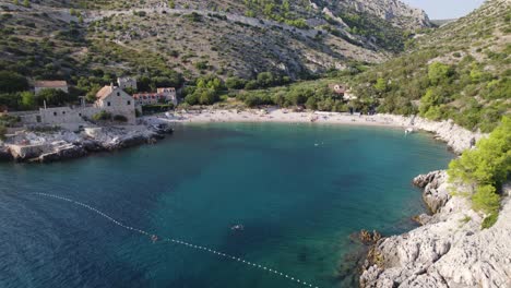 Aerial-view-of-Dubovica-Beach,-Hvar,-with-village-and-sunlit-shores