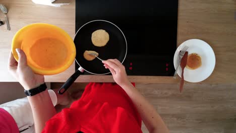 top-down-shot-of-female-hands-making-pancakes-on-a-hot-black-pan-on-electric-stove