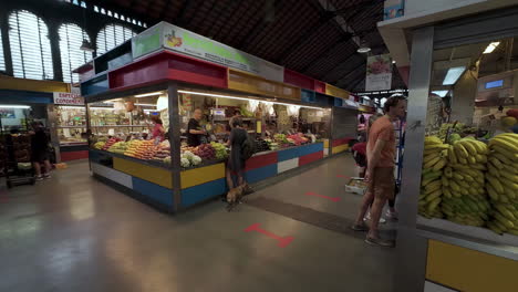 Slow-motion-shot-of-vendor-assisting-shoppers-choosing-ripe-organic-fruits-and-vegetables-in-an-indoor-local-market