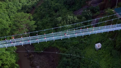 Aerial-View-Of-People-Walking-In-The-Glass-Bottomed-Bridge-That-Connected-Blangsinga-Traditional-Village-And-Tegenungan-Waterfall-In-Bali,-Indonesia