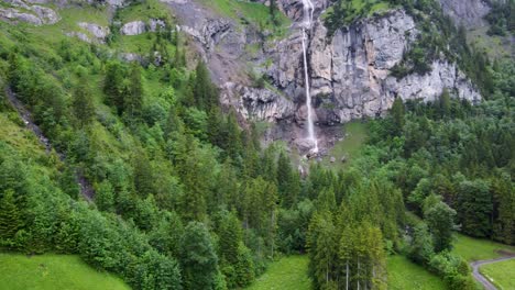 Almenbachfall-waterfall-flowing-through-pinewood-and-alpine-rocks-in-Kandersteg-Switzerland,-Aerial
