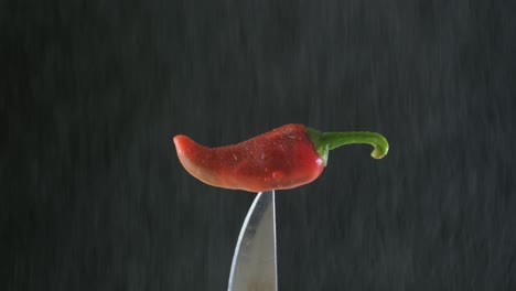 Red-chili-pepper-stuck-in-a-knife-with-water-drizzling-on-a-black-background