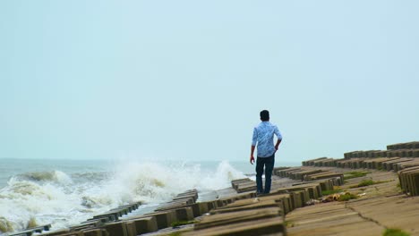 Lone-Man-Lighting-Cigarette-While-Walking-Over-The-Coast-With-Block-Stone-Breakwater