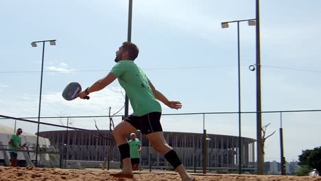 Man-plays-serving-ball-on-padel-beach-tennis-court