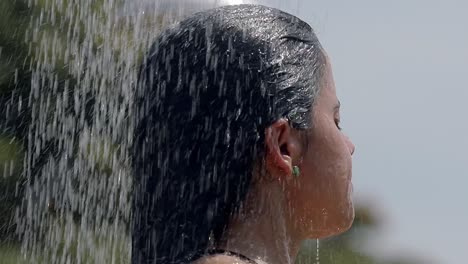 woman-showering-on-the-beach,-head-shot-close-up,-latin-dark-hair,-earring,-hands-through-hair,-washing-hair,-tilt-down-shot