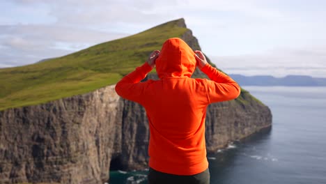 Man-putting-on-hoodie-and-opening-his-arms-at-Traelanipa-cliff,-freedom-concept