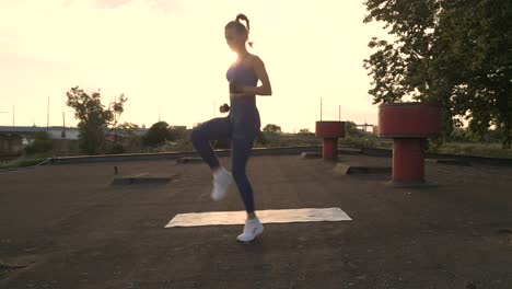 Eine-Fitnessfrau-Läuft-Auf-Der-Stelle-Und-Hebt-Ihre-Knie-Hoch,-Während-Die-Sonne-Untergeht