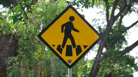 Pedestrian-crossing-sign-with-lush-green-tree-leaves-on-the-background
