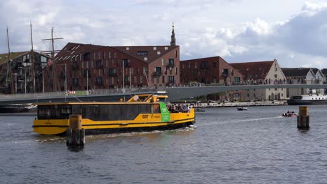 Busy-day-at-at-canals-and-inner-harbor-bridge-in-Copenhagen-Denmark---Yellow-taxi-boat-sailing-forward-and-lots-of-people-walking-across-bridge