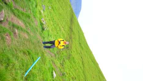 Man-standing-on-grassy-hillside-piloting-drone-with-remote-control-at-Faroe-Islands