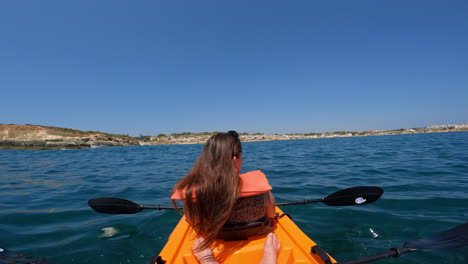 Woman-wearing-sunglasses-on-her-head-sways-in-a-kayak-on-the-clear-blue-waters-of-Malta