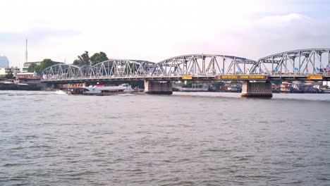 A-river-cruise-boat-is-about-to-pass-beneath-the-Krung-Thon-Bridge-spanning-the-Chao-Phraya-river,-a-gateway-to-major-tourist-attractions-in-Bangkok,-Thailand