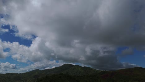 Dense-clouds-moving-over-the-forested-hills-during-the-day-covering-blue-sky