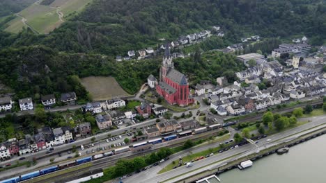 Freight-train-transporting-Cargo-through-Oberwesel-town-past-Red-Church-of-our-Lady-along-River-Rhine