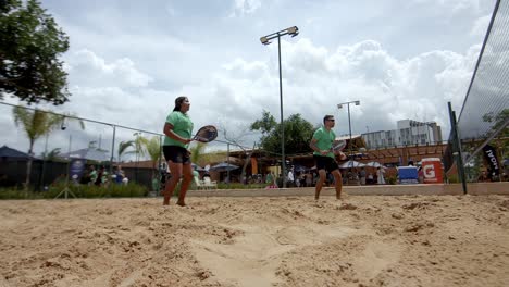 Jugadores-Masculinos-Y-Femeninos-Saltando-Para-Alcanzar-Y-Ganar-El-Punto-De-Tenis-Playa.