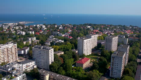 Aerial-backwards-shot-of-residential-apartments-in-park-of-Gdynia-with-blue-Baltic-Sea-and-cruising-ships-in-background