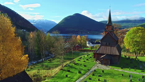 Aerial-view-passing-a-stave-church,-fall-foliage-in-the-fjords-of-Central-Norway