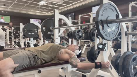 Asian-man-with-headphones-on-performing-bench-press-in-gym