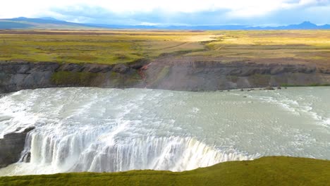Aerial-drone-tracking-shot-over-a-large-Icelandic-plain-with-a-river-in-the-foreground-and-a-large-impressive-waterfall-called-gulfoss