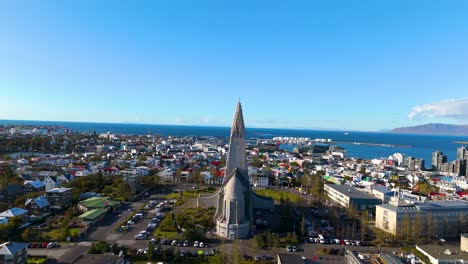 drone-shot-of-a-beautiful-and-impressive-church,-the-Hallgrímskirkja,-in-the-capital-of-Islance-Reykjavik,-with-the-city-all-around,-the-sea-in-the-background-and-sunny-weather
