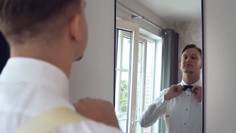 Young-caucasian-man-looking-in-the-mirror-and-preparing-himself-for-his-wedding-ceremony