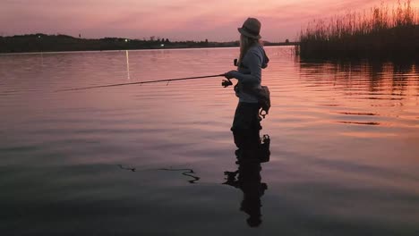 Ein-Schönes-Mädchen,-Das-Nach-Sonnenuntergang-In-Einem-Ruhigen-See-Fischt