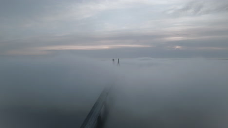 Car-starting-trip-in-early-foggy-morning-on-bridge-hiding-in-mist,-aerial-view