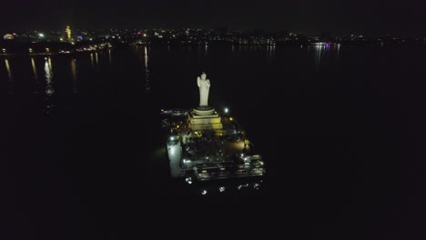 A-cinematic-aerial-shot-of-Hussain-Sagar-Lake,-Hyderabad's-most-well-known-landmark,-at-night-Indian-monolith-known-as-the-Buddha-Statue-of-Hyderabad