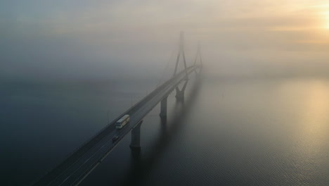Overnight-bus-journey-over-foggy-bridge-during-sunrise,-aerial-view