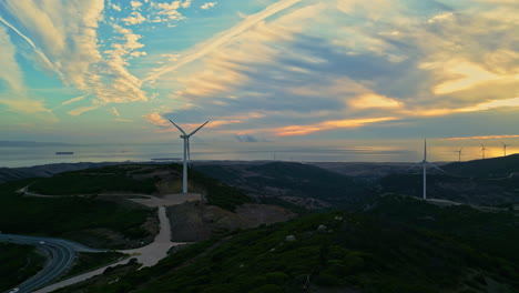 Wind-turbines-overlook-ocean-on-hillside,-beautiful-yellow-cloudy-sky-at-golden-hour