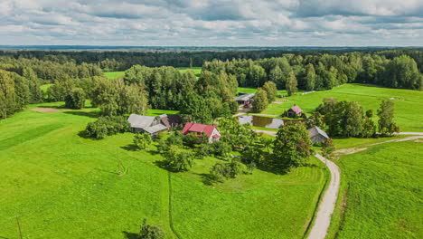 Aerial-hyper-lapse-pushes-in-to-homestead-house-by-pond-in-countryside,-cloud-shadows-pass-over