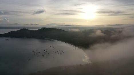 Drone-soars-above-clouds-down-on-Playa-Hermosa-Costa-Rica-at-sunrise,-cinematic