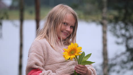 Süßes-Kleines-Mädchen-Hält-Sonnenblume-In-Der-Hand-Und-Lächelt,-Porträtansicht