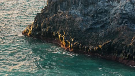 Golden-hour-glow-spread-across-eroded-sea-cliffs-of-Los-Gigantes-Tenerife-as-waves-crash-on-rocks