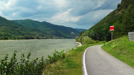 Two-Cyclists-Pass-By-Bicycle-Trail-near-The-Danube-River