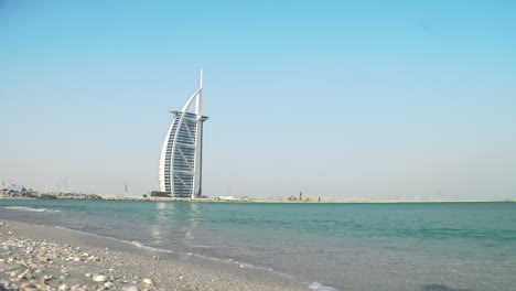 Burj-Al-Arab-Vom-Jumeira-Strand-Aus-Gesehen,-Friedlicher,-Windiger-Strand,-Wellen,-Blauer-Himmel,-Blaues-Meer-Usw