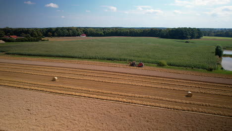 Aerial-parallax-around-tractor-and-hay-bales-on-empty-dry-agriculture-fields,-blue-sky